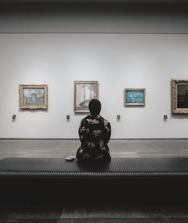 A woman sitting in an art gallery, observing and admiring the displayed paintings