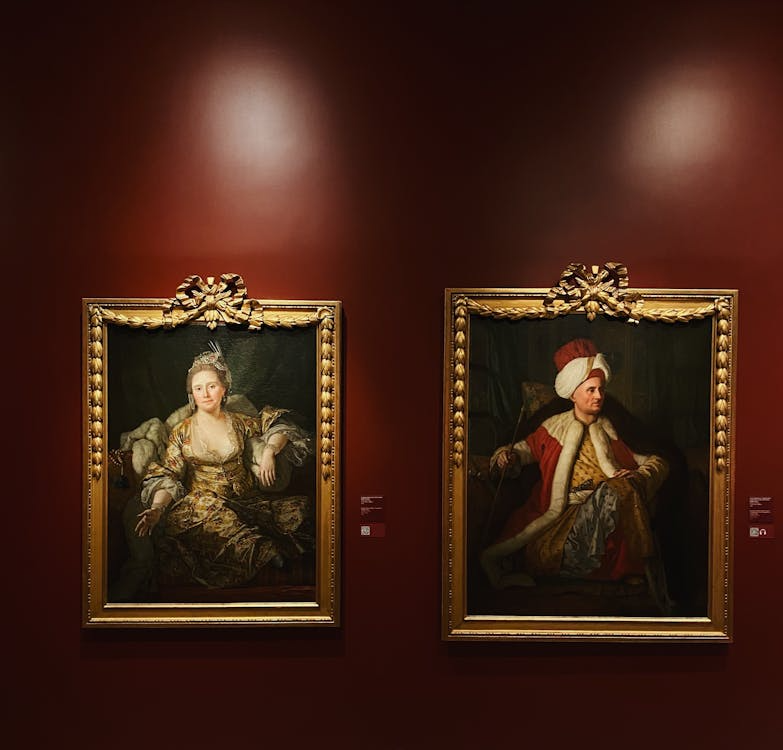 Two ornate gold-framed portrait paintings displayed in a gallery, representing high-value art collections.