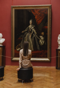 A woman sitting in an art gallery while admiring a framed painting