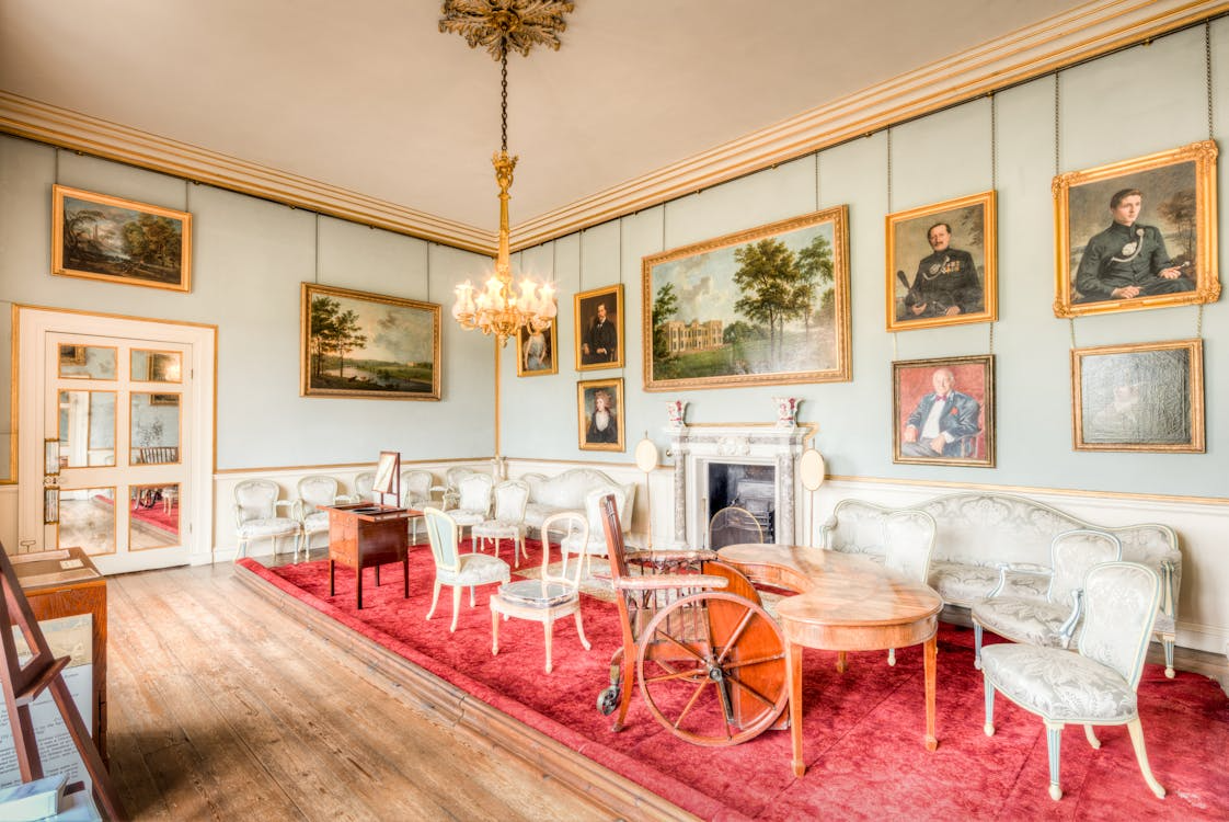 A grand estate room displaying multiple gold-framed portrait paintings alongside period furniture.