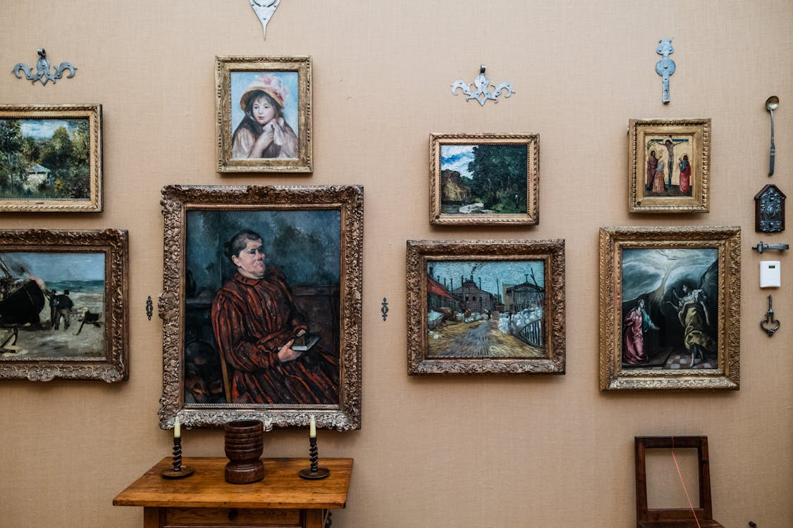 A curated wall of diverse gold-framed paintings, including portraits and landscapes.