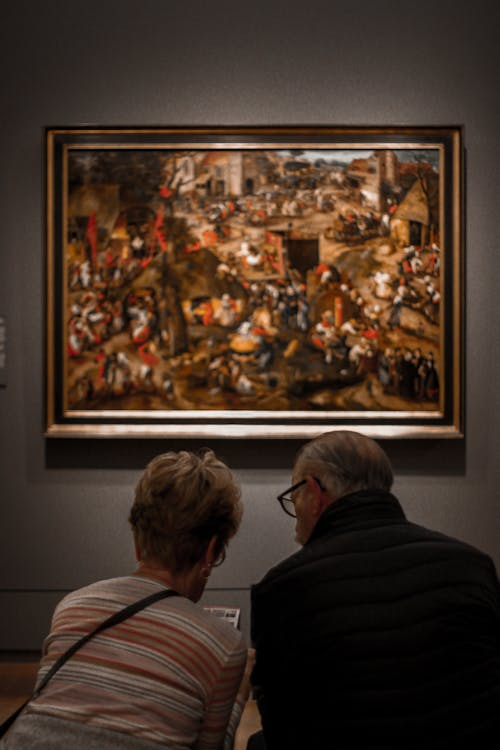 A man and a woman sitting together inside an art gallery, observing the displayed artwork