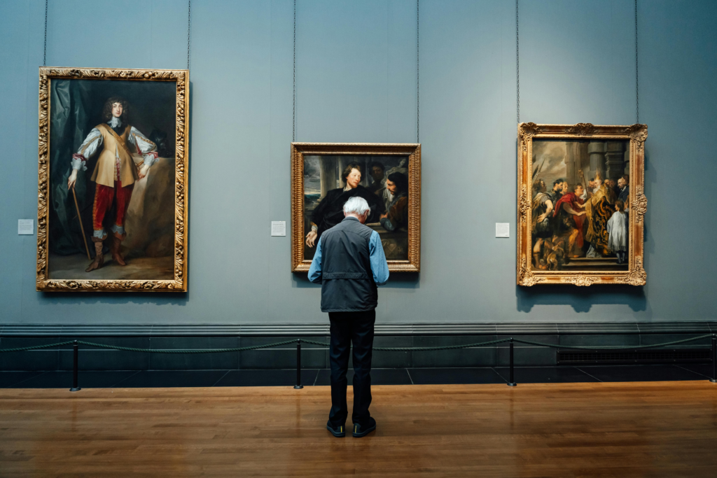 A man standing inside an art gallery viewing the exhibited artworks on the walls