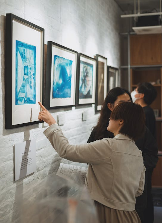 Woman in an art gallery pointing at a painting while holding a document