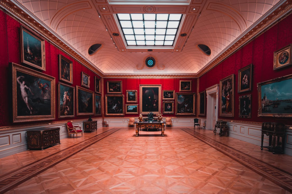 A grand museum gallery with floor-to-ceiling gold-framed paintings on red walls.