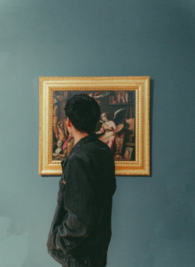 A man closely observing a framed painting in an art gallery