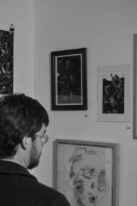 Grayscale image of a man observing paintings in an art gallery