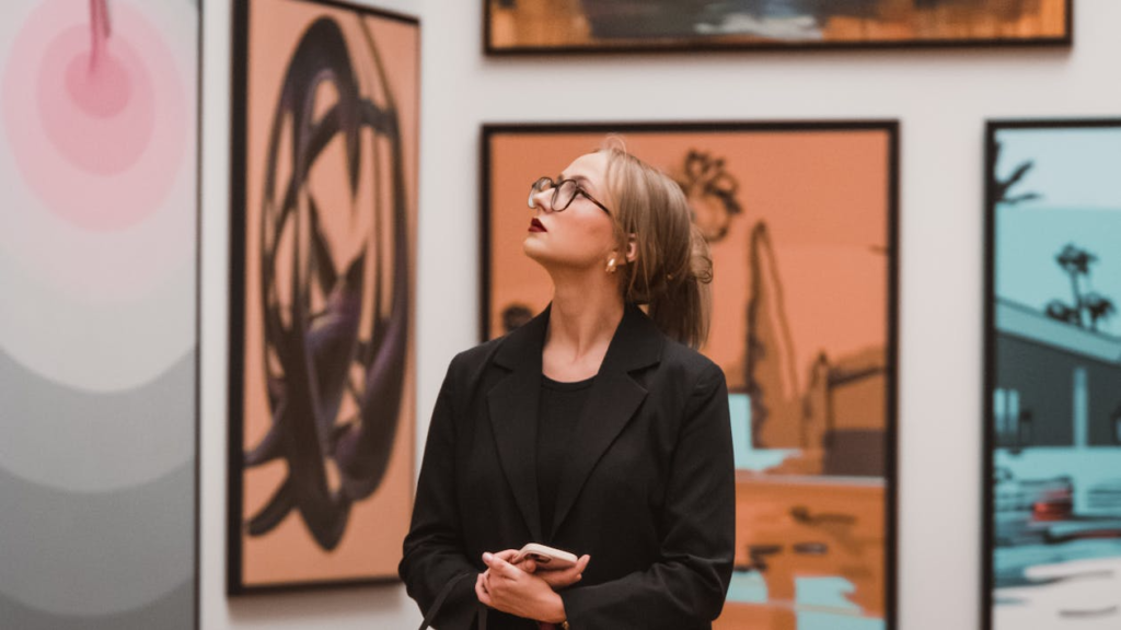 A woman standing inside an art gallery with framed paintings displayed in the background