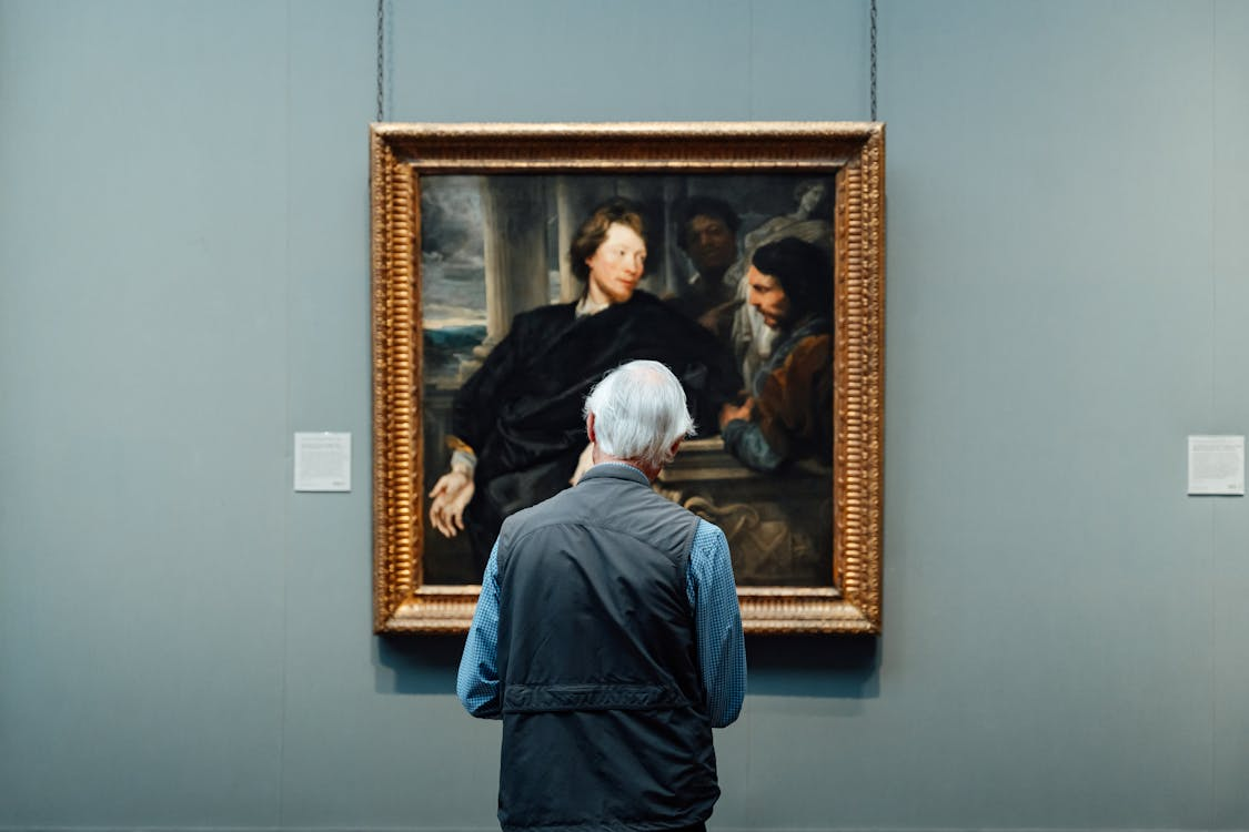 A collector studying a gold-framed old master portrait in a museum gallery.