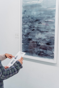 Person pointing at a paper next to an abstract painting on display