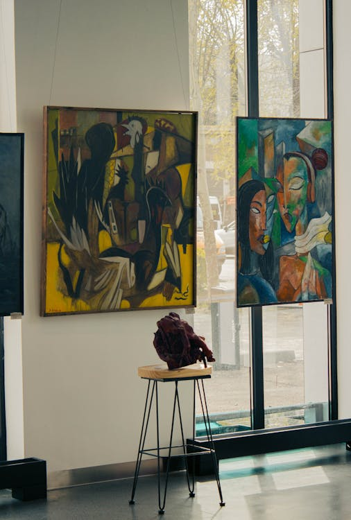 A gallery wall displaying multiple framed paintings in an exhibition setting
