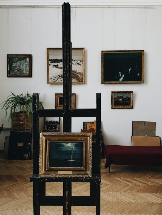 Paintings displayed on a gallery wall, with one artwork placed on a stand in the foreground